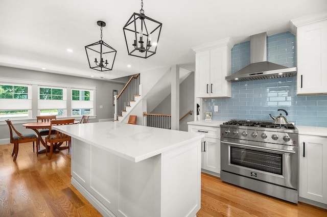 kitchen featuring decorative light fixtures, white cabinetry, high end stainless steel range oven, a center island, and wall chimney range hood