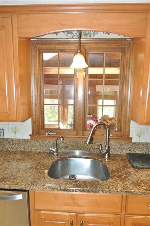 kitchen featuring dishwasher, dark stone countertops, tasteful backsplash, and a sink