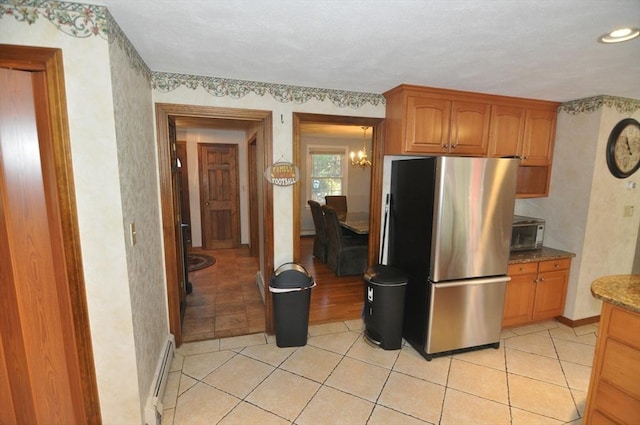 kitchen with stone counters, brown cabinets, freestanding refrigerator, a baseboard radiator, and light tile patterned flooring