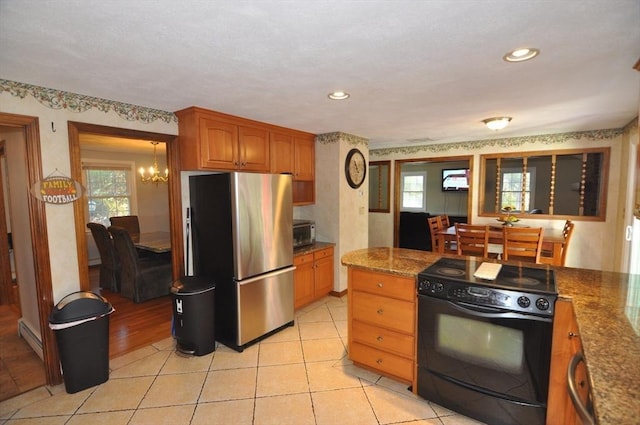 kitchen with brown cabinets, a baseboard heating unit, freestanding refrigerator, electric range, and a notable chandelier
