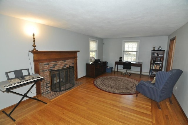 living area with baseboards, a brick fireplace, and wood finished floors
