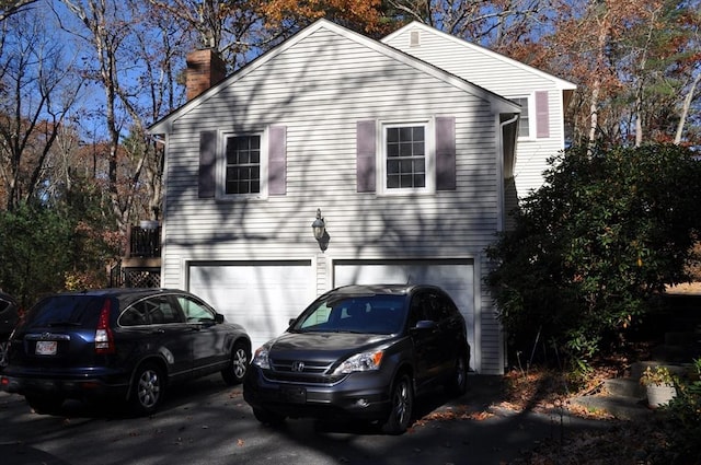 view of property exterior with an attached garage, driveway, and a chimney