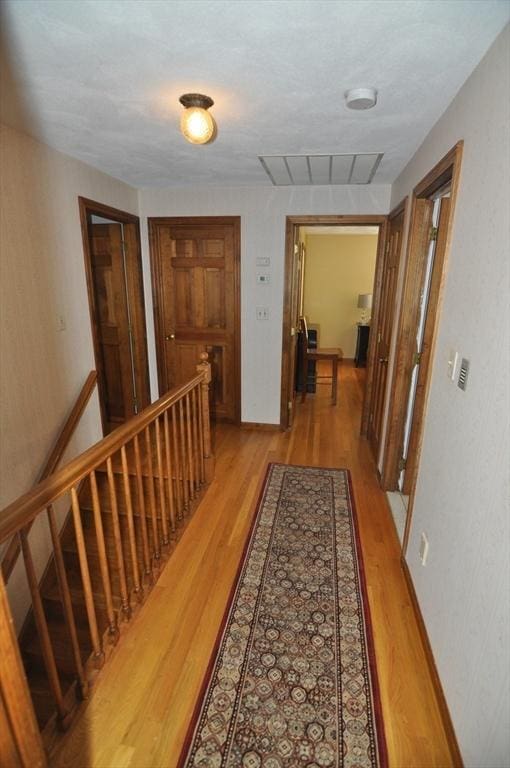 hallway featuring an upstairs landing, baseboards, light wood-type flooring, and visible vents