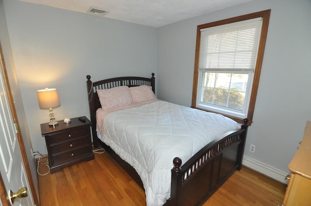 bedroom with baseboards, visible vents, wood finished floors, and baseboard heating