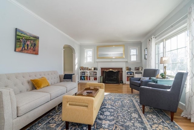 living room with wood-type flooring, a brick fireplace, and ornamental molding