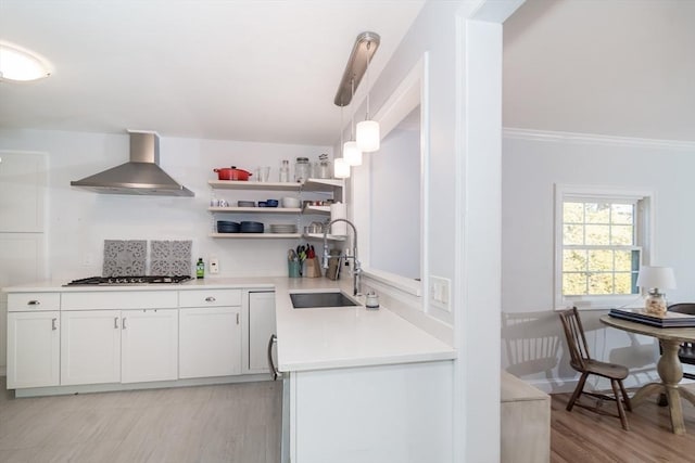 kitchen with sink, stainless steel gas cooktop, decorative light fixtures, wall chimney range hood, and white cabinets