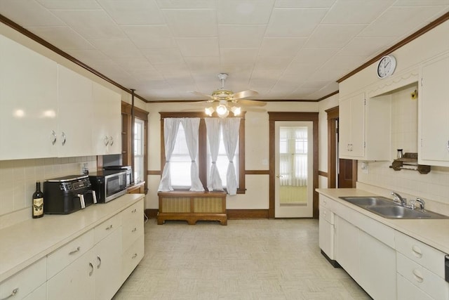 kitchen featuring a sink, white cabinets, light countertops, ornamental molding, and stainless steel microwave