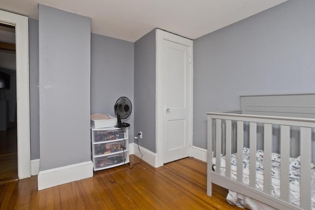 bedroom with a crib, baseboards, and wood finished floors