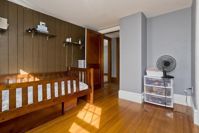 bedroom with baseboards, wood walls, and light wood finished floors