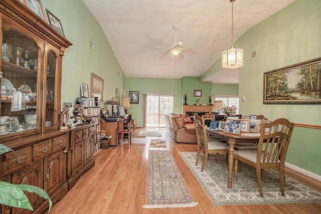 dining room with high vaulted ceiling, a fireplace, ceiling fan, and light wood-style flooring