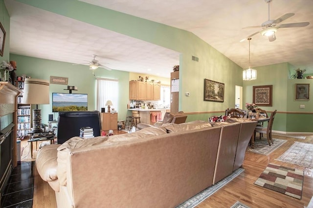 living area featuring light wood finished floors, lofted ceiling, visible vents, baseboards, and ceiling fan with notable chandelier