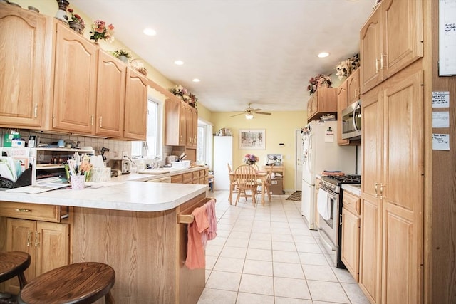 kitchen with light tile patterned floors, a kitchen breakfast bar, a peninsula, stainless steel appliances, and light countertops