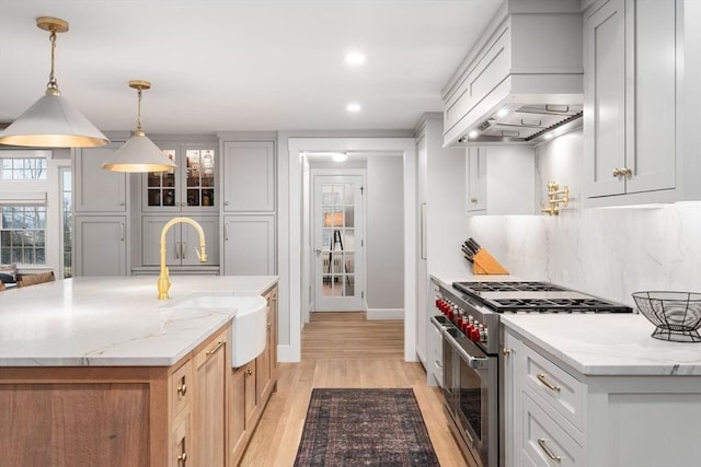 kitchen with premium range hood, high end stainless steel range, an island with sink, and hanging light fixtures