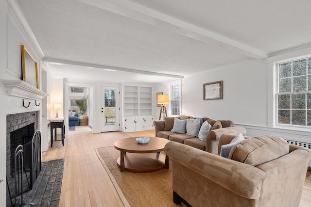 living room featuring beamed ceiling, plenty of natural light, wood-type flooring, and a brick fireplace