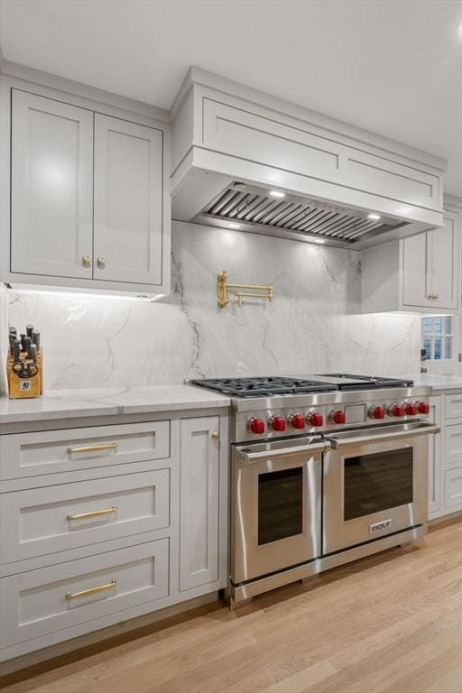 kitchen featuring custom range hood, decorative backsplash, light hardwood / wood-style floors, and designer stove