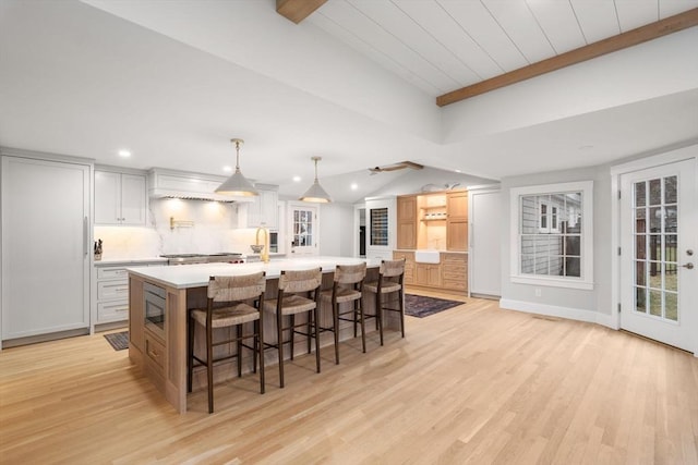 kitchen with a spacious island, vaulted ceiling with beams, decorative light fixtures, light hardwood / wood-style floors, and white cabinets