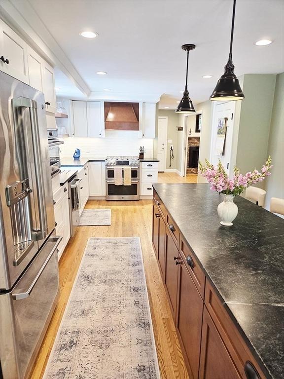 15 Sudbury Rd, Stow, MA 01775 - kitchen featuring premium appliances, custom range hood, light wood-style floors, white cabinetry, and decorative light fixtures
