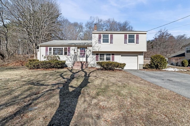 tri-level home with a garage, driveway, a front yard, and a chimney