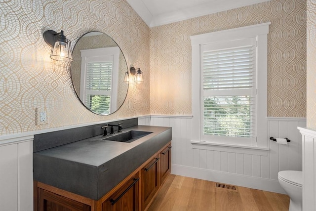 bathroom with visible vents, wainscoting, wood finished floors, and wallpapered walls