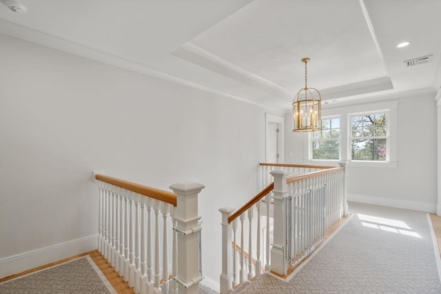corridor with visible vents, baseboards, a tray ceiling, a chandelier, and an upstairs landing