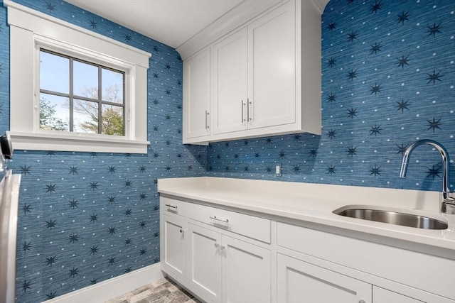 clothes washing area with baseboards, wallpapered walls, and a sink