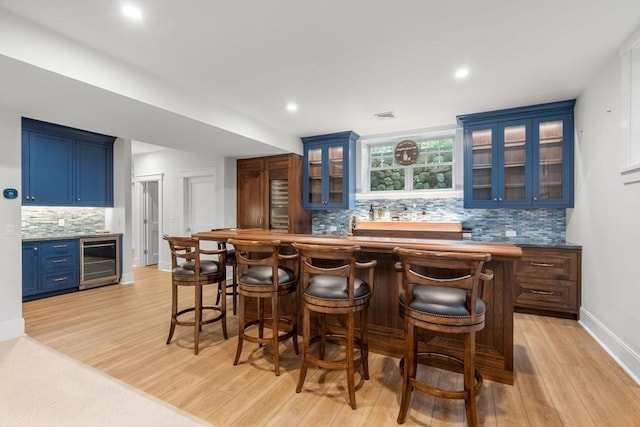 bar featuring indoor wet bar, backsplash, light wood-type flooring, and wine cooler