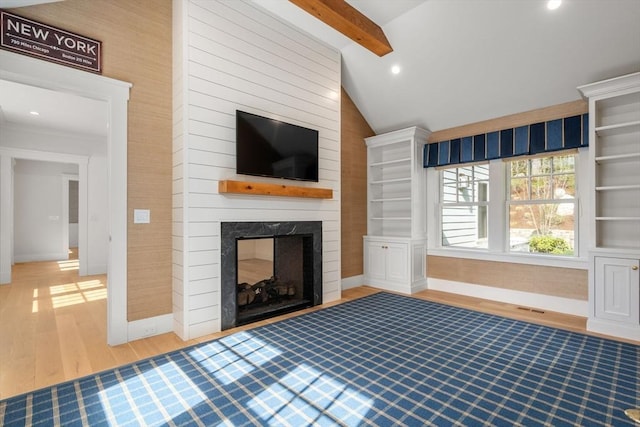 unfurnished living room featuring visible vents, wood finished floors, baseboards, lofted ceiling with beams, and a premium fireplace