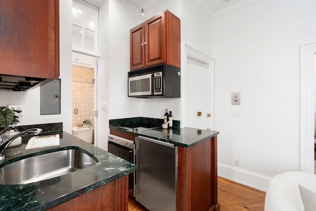 kitchen featuring light hardwood / wood-style floors, crown molding, dark stone countertops, appliances with stainless steel finishes, and sink