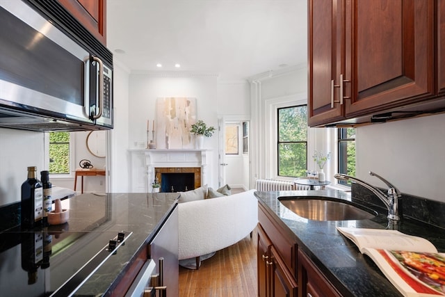 kitchen featuring light hardwood / wood-style flooring, crown molding, a fireplace, dark stone countertops, and sink