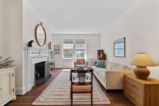 living area featuring radiator heating unit, dark wood-style flooring, a fireplace with flush hearth, and baseboards