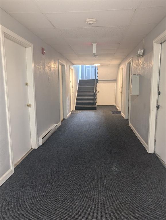 300 Smithfield Rd Unit 2-2, North Providence, RI 02904 - hallway featuring a baseboard heating unit, stairway, dark carpet, a paneled ceiling, and baseboards