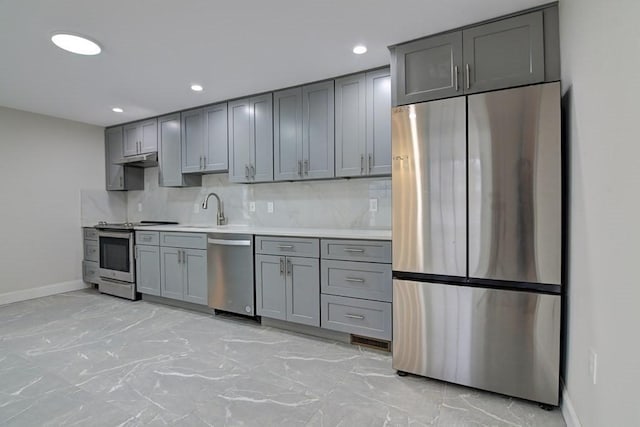kitchen with light countertops, stainless steel appliances, baseboards, backsplash, and gray cabinetry