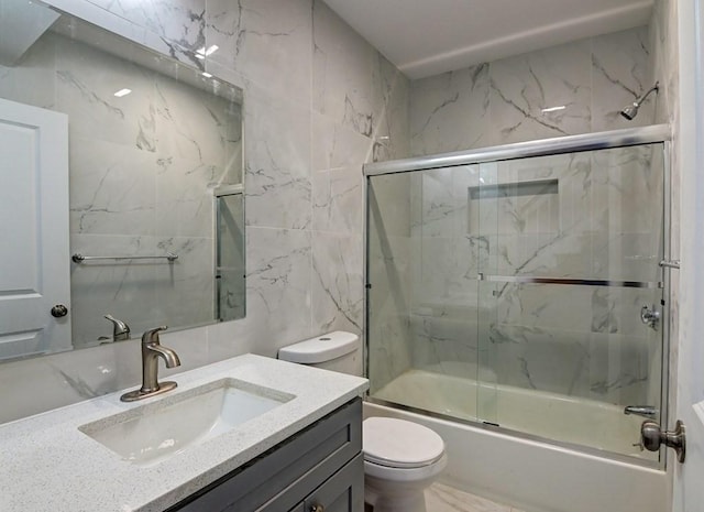 full bath with tile walls, vanity, bath / shower combo with glass door, toilet, and marble finish floor