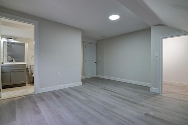 interior space with baseboards, a sink, light wood finished floors, and vaulted ceiling