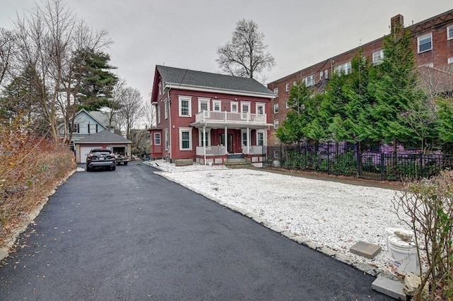 colonial-style house with fence, covered porch, an outbuilding, and a balcony
