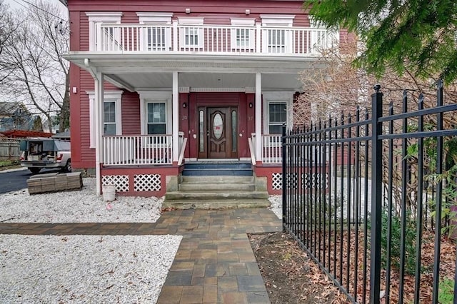 view of exterior entry featuring fence, covered porch, and a balcony