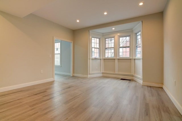 empty room with baseboards, recessed lighting, light wood finished floors, and a wealth of natural light