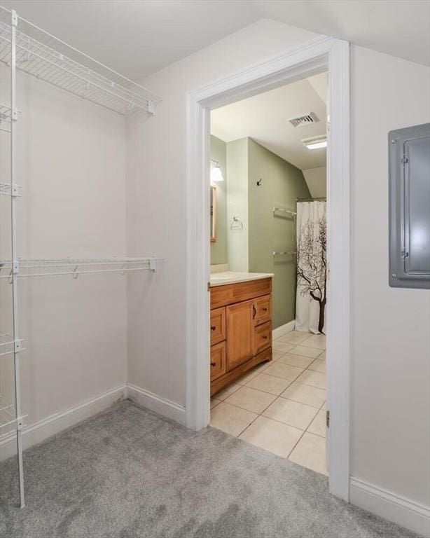 spacious closet featuring light carpet, electric panel, visible vents, vaulted ceiling, and light tile patterned flooring