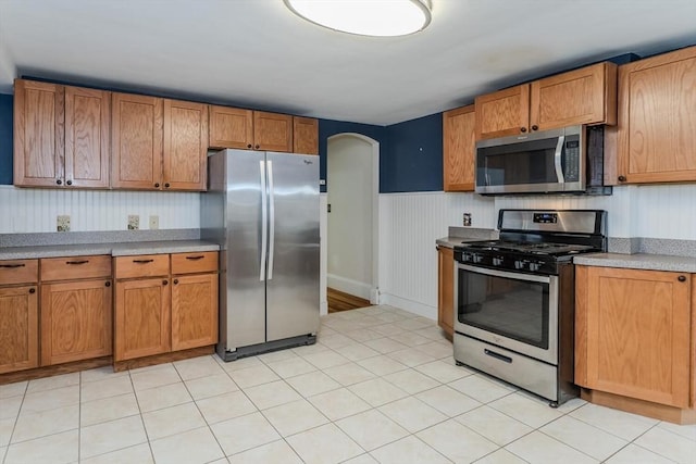 kitchen featuring stainless steel appliances, wainscoting, and brown cabinetry