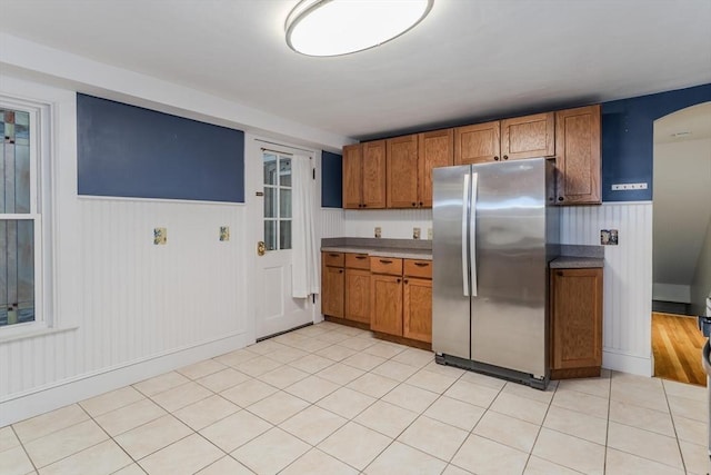 kitchen featuring a wainscoted wall, light tile patterned flooring, brown cabinets, and freestanding refrigerator