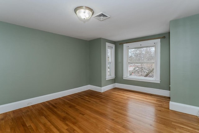 spare room featuring baseboards, visible vents, and wood finished floors