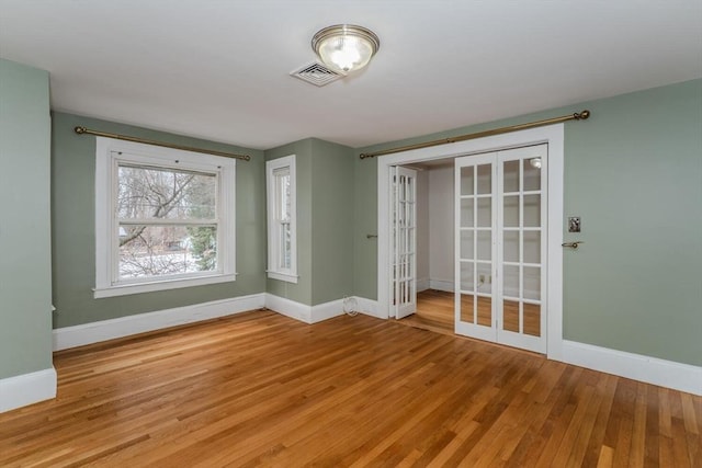 empty room with french doors, wood finished floors, visible vents, and baseboards