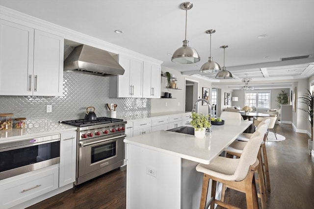 kitchen featuring a center island with sink, appliances with stainless steel finishes, pendant lighting, wall chimney exhaust hood, and sink