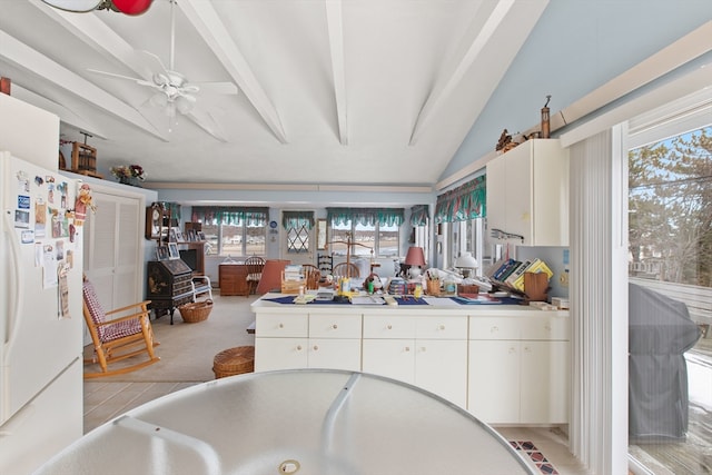 kitchen featuring lofted ceiling with beams, light carpet, white fridge, ceiling fan, and white cabinets