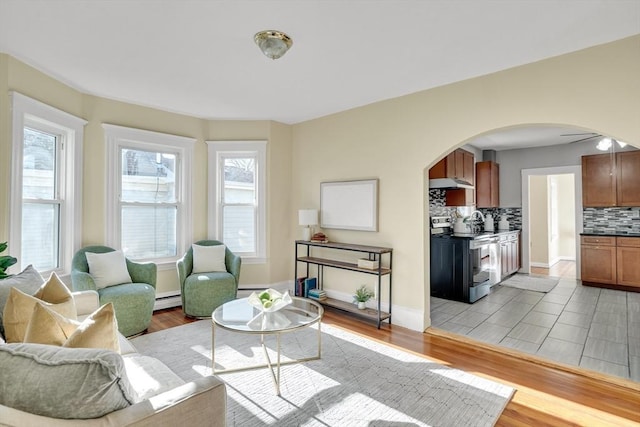 living room with ceiling fan, a baseboard heating unit, and light hardwood / wood-style flooring