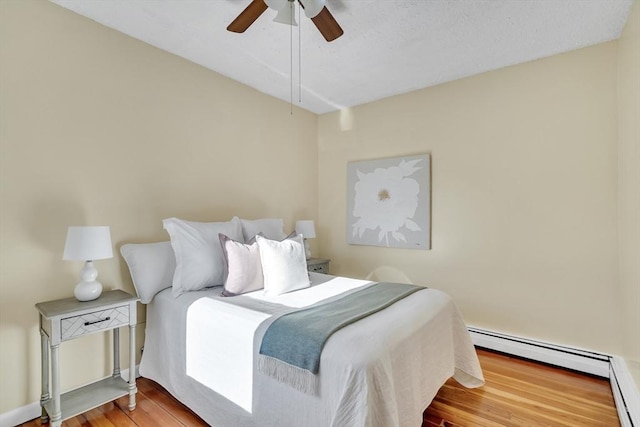 bedroom with ceiling fan, wood-type flooring, and a baseboard radiator