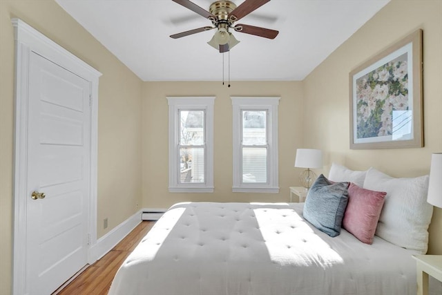 bedroom featuring ceiling fan, light hardwood / wood-style flooring, and a baseboard heating unit