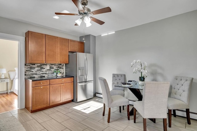 kitchen with ceiling fan, a baseboard heating unit, stainless steel fridge, decorative backsplash, and light wood-type flooring