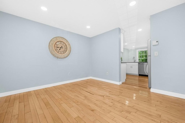 empty room featuring light wood-style floors, a sink, baseboards, and recessed lighting