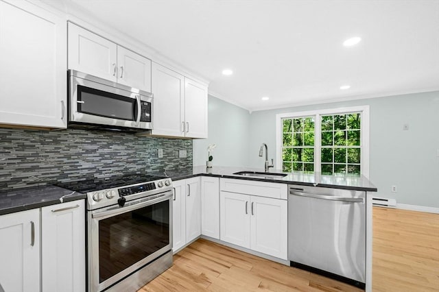 kitchen featuring stainless steel appliances, a sink, a baseboard heating unit, a peninsula, and backsplash